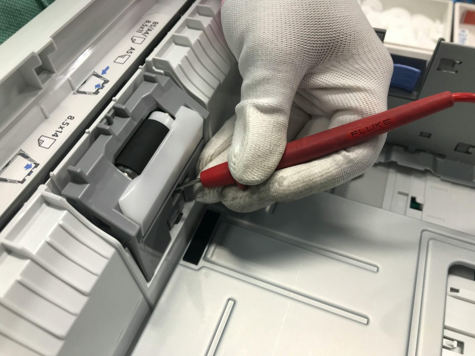 A gloved hand fixes a printer using a red precision tool, showcasing maintenance skills.